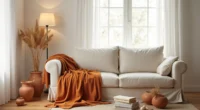 Rust throw blanket draped over sofa arm with terra-cotta vessels, wheat stalks, and cream napkins on wood floor.