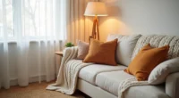 A sofa corner layered with a chunky knit throw, rust and gold patterned pillows, and a warm neutral woven area rug.