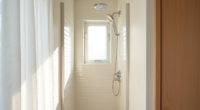 White-tiled shower corner with chrome showerhead and narrow stall space lit by natural window light.