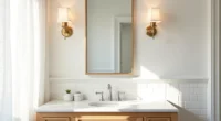 Brass sconces flank a rectangular mirror above a marble vanity with subway tile walls and chrome faucet.