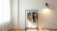 Black metal clothing rack with eight hanging garments in a bright corner against white wall and hardwood floor.