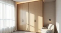 Floor-to-ceiling matte oak wardrobe with recessed top lighting, polished concrete floor, and a linen chair in a minimalist